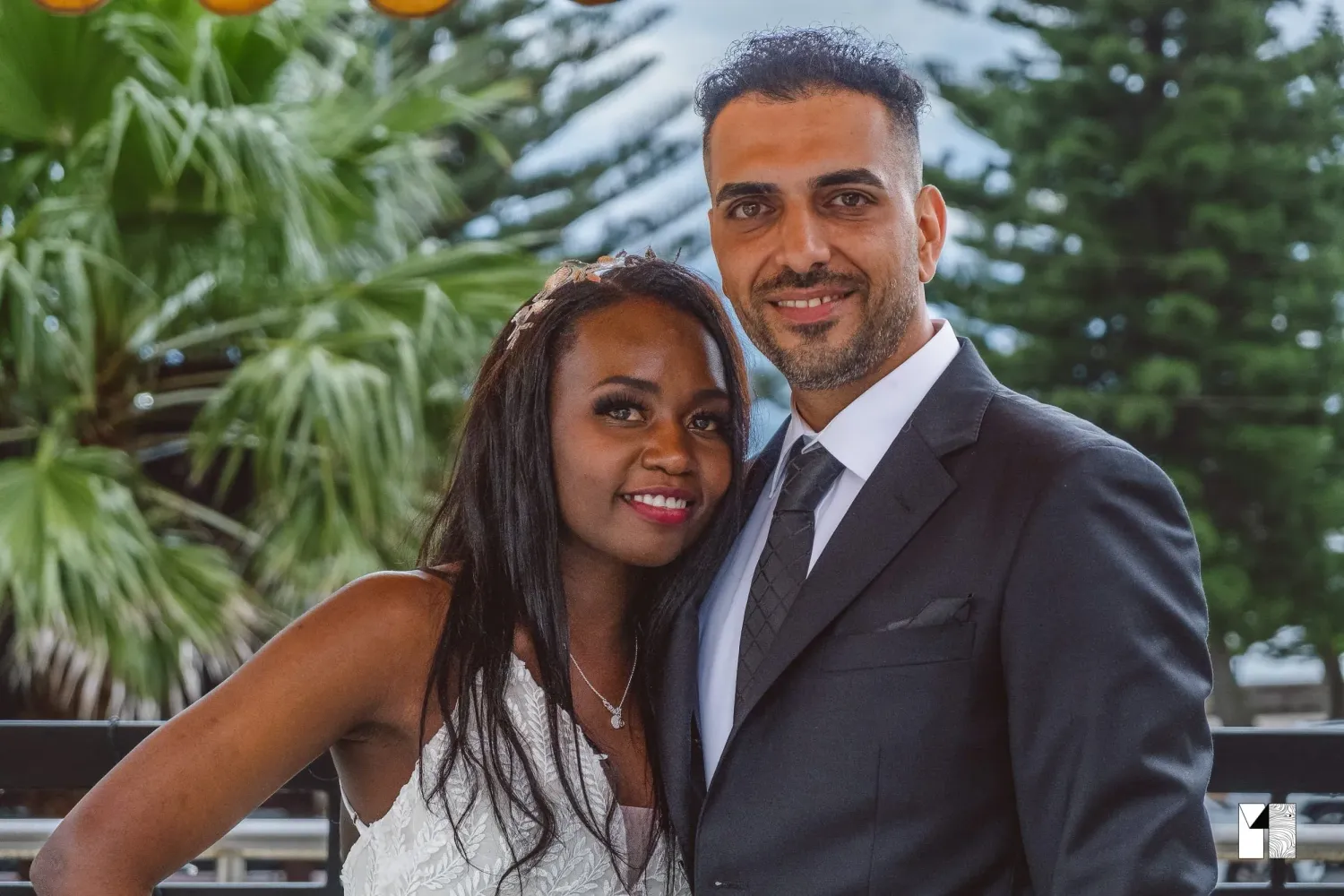 Smiling couple posing together in front of tropical greenery at wedding.