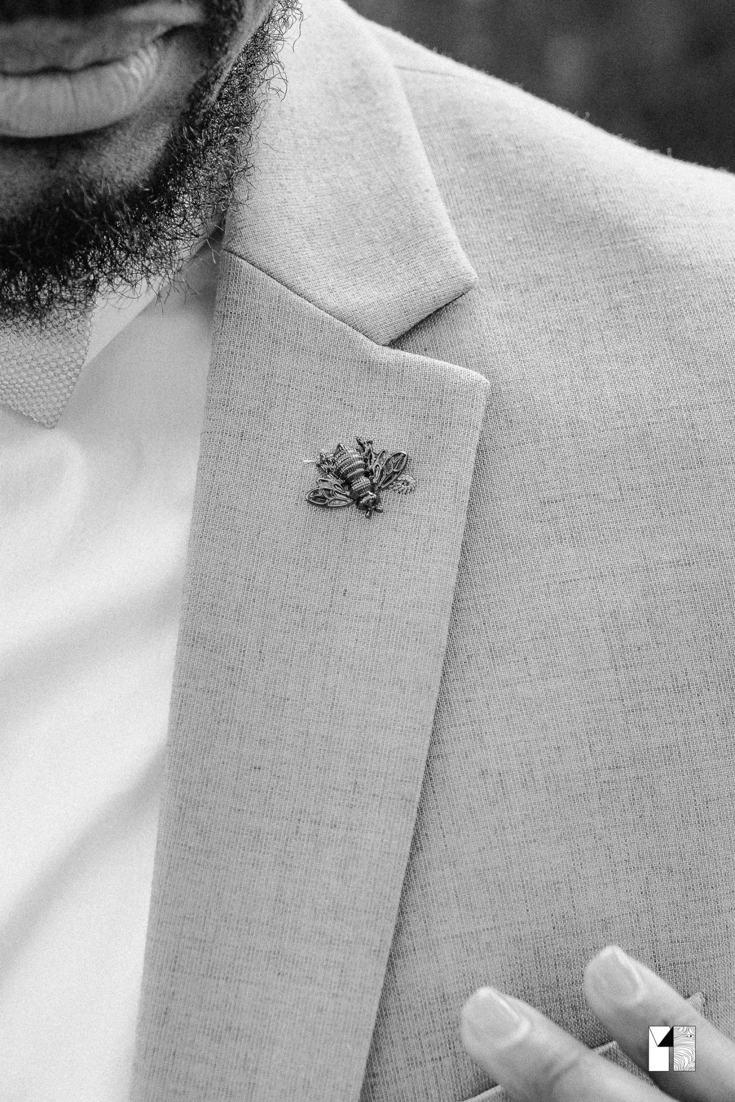 Close-up of a bee lapel pin on a light gray suit jacket worn by a groom.