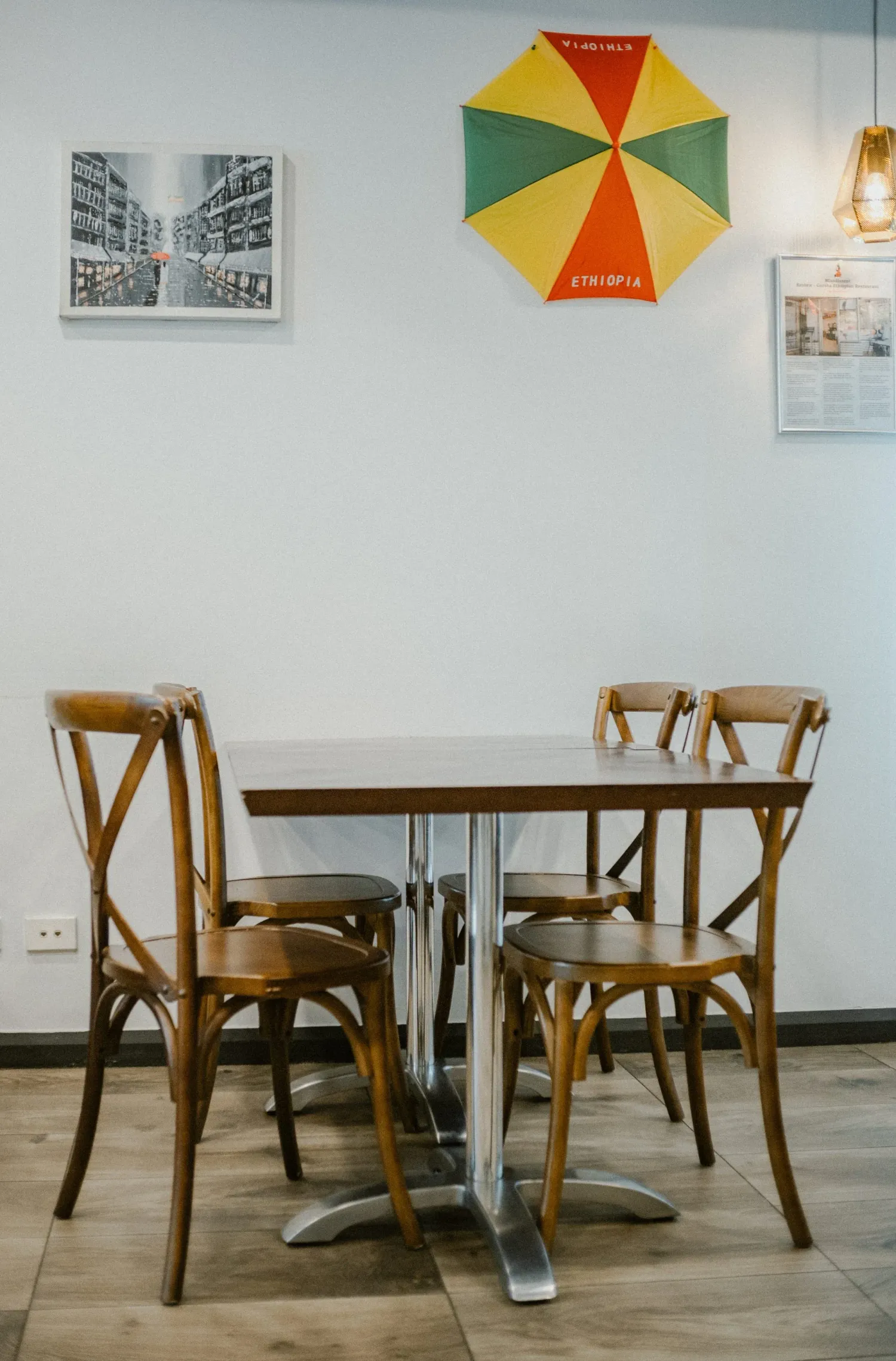 Cozy Ethiopian restaurant interior with wooden chairs, a table, and a colorful Ethiopia umbrella wall decor.