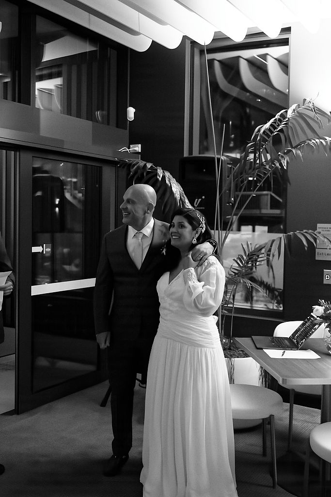 Black and white portrait of a smiling bride in a white gown and groom in a suit standing together indoors.
