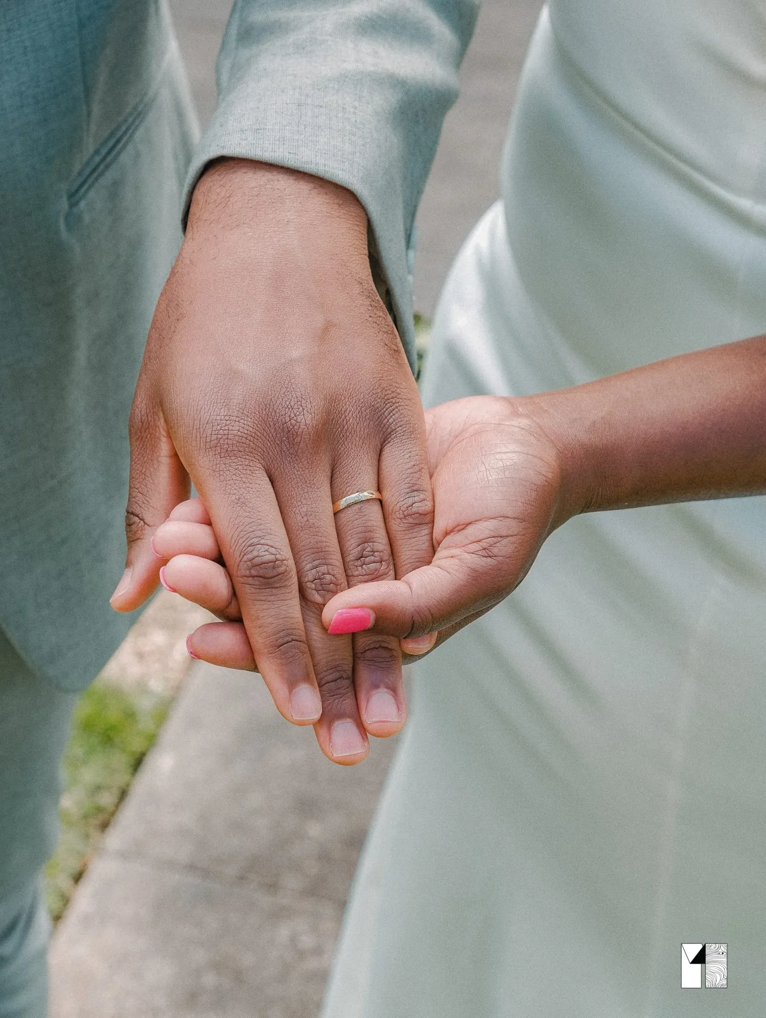 Close-up of newlywed couple holding hands showing gold wedding band and pink manicured nails.