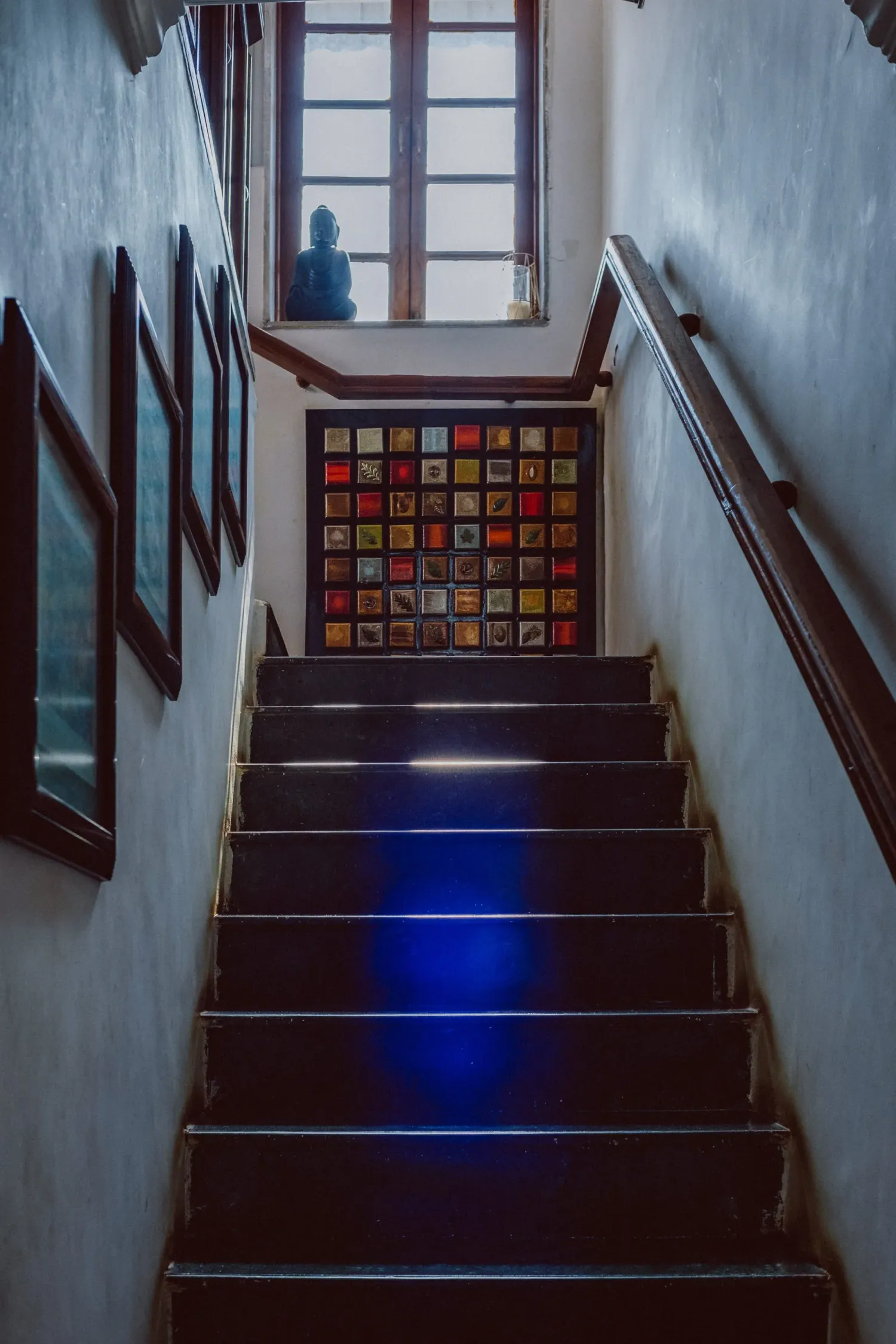 Narrow wooden staircase leading to colorful stained glass window with blue light reflection on steps.