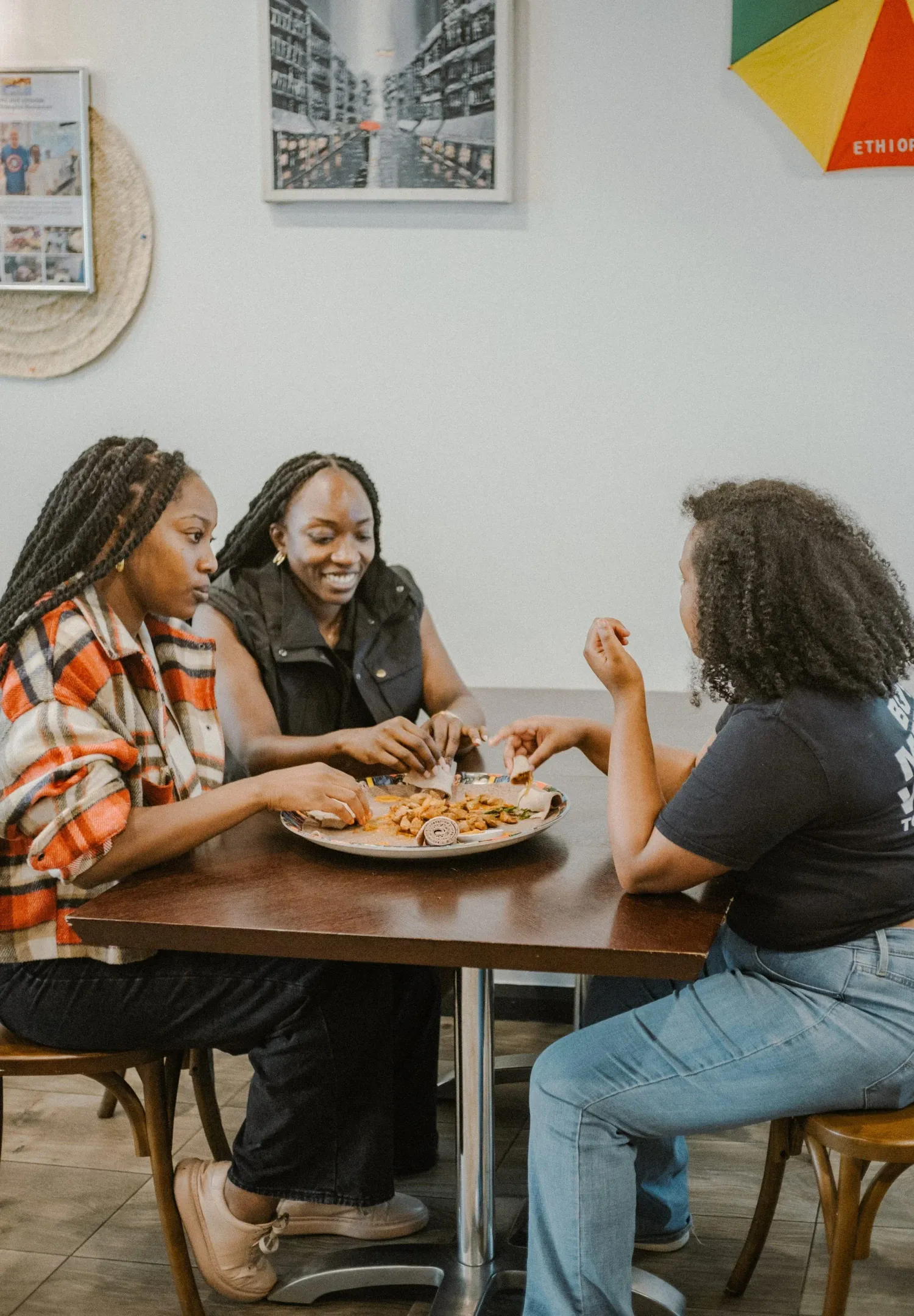 Three women sharing a meal together at a wooden table in a casual Ethiopian restaurant.