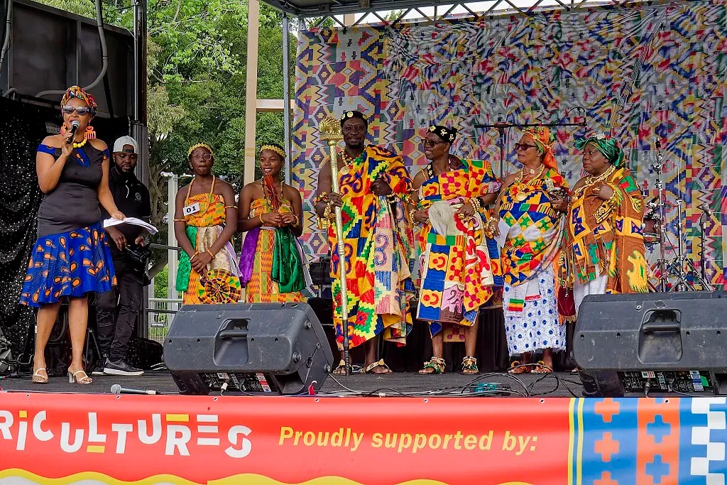Group of performers in colorful African kente cloth costumes on stage at Aficultures festival.