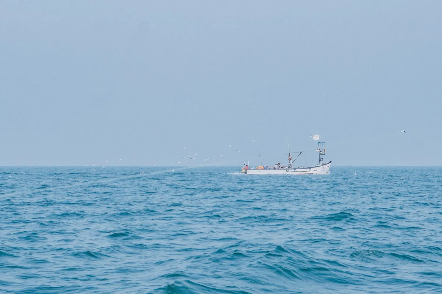 Cargo ship sailing on calm blue ocean waters under hazy sky in open sea.