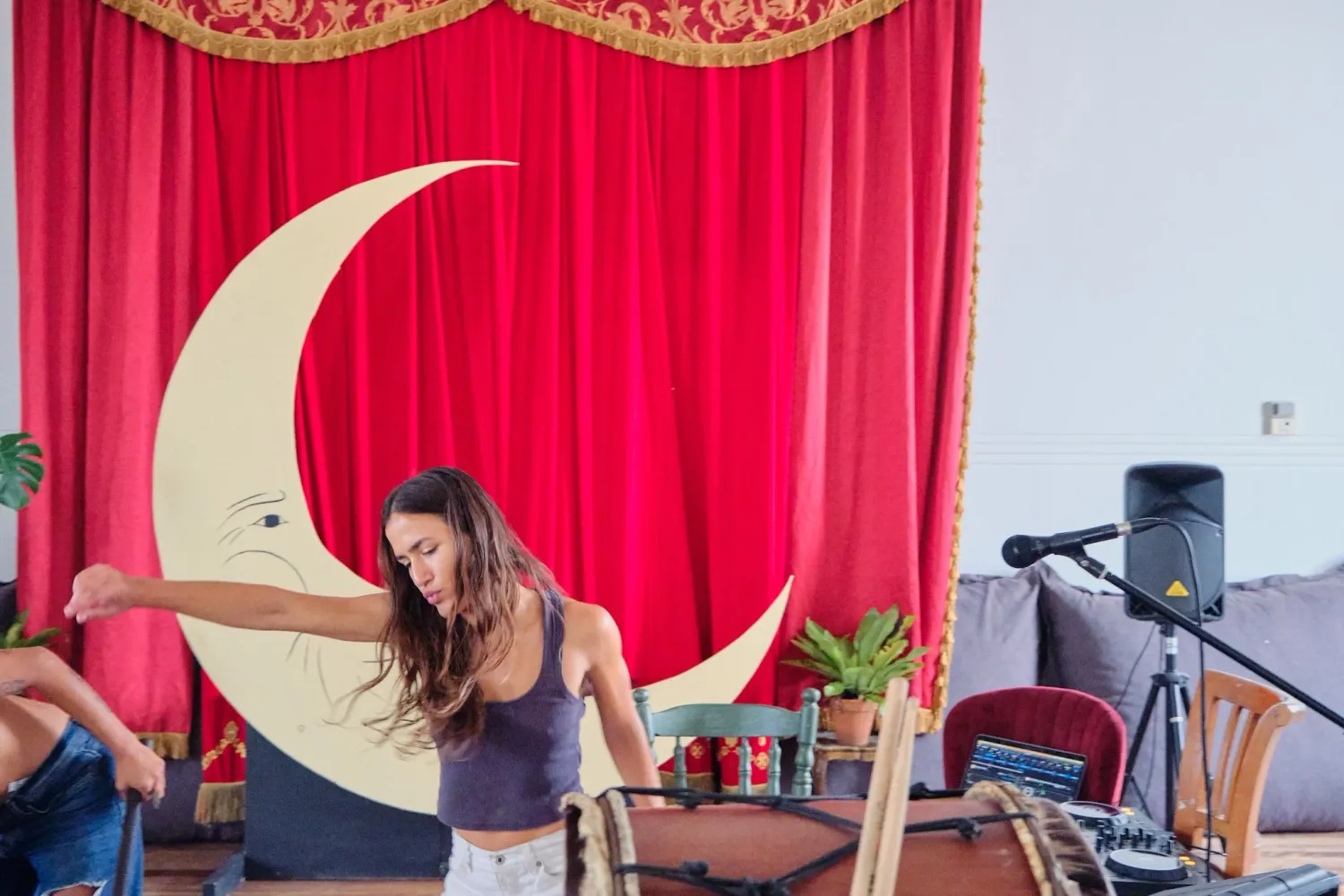 Female dancer performing energetically in front of red curtain with decorative crescent moon backdrop.
