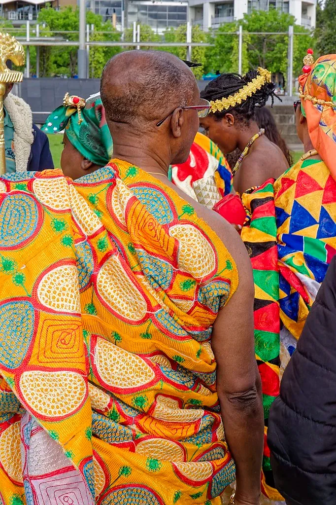 Man in elaborate orange African kente cloth robe at colorful cultural celebration outdoors.