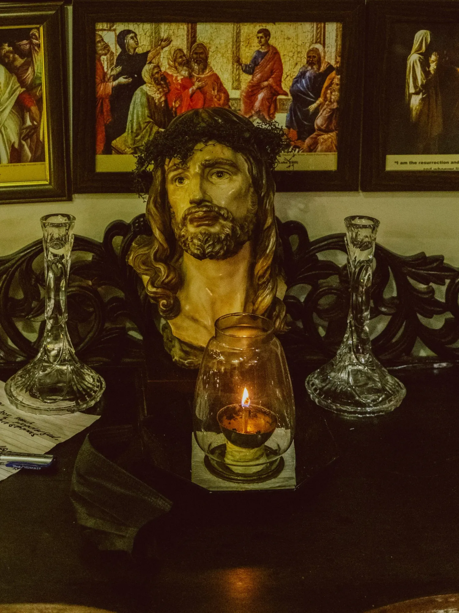 Religious bust sculpture of Jesus Christ with crown of thorns beside lit candle and crystal candleholders.