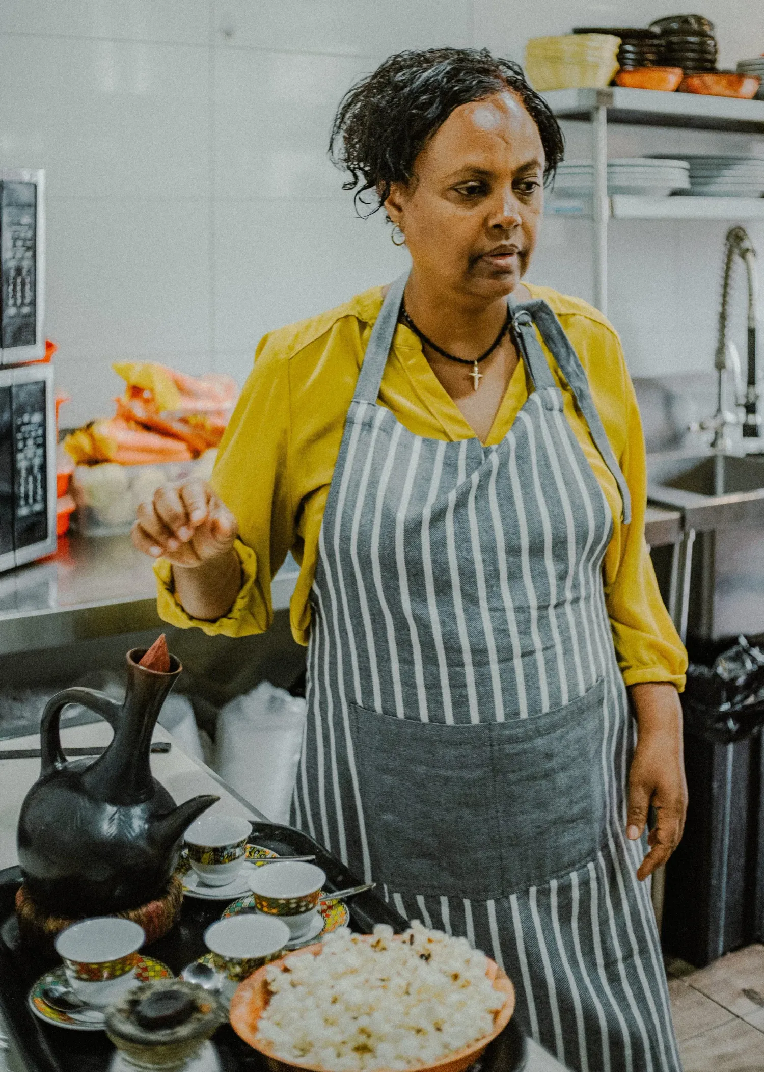 Ethiopian woman in striped apron preparing traditional coffee ceremony with jebena pot and popcorn.