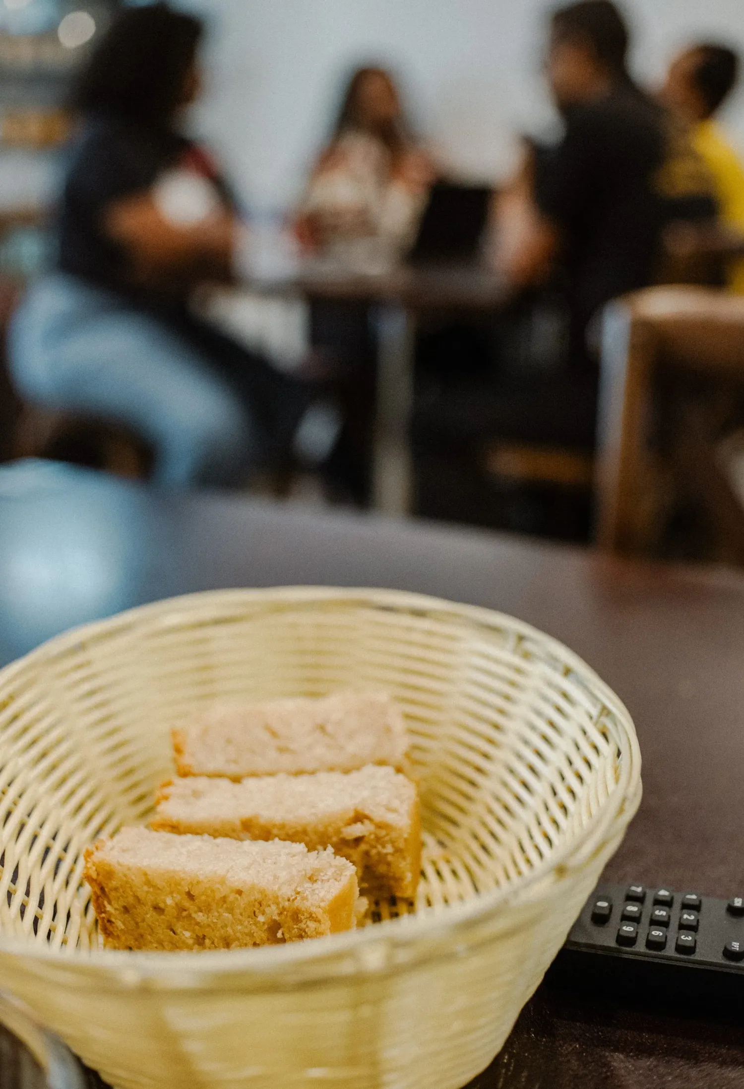 Sliced bread pieces in a woven basket on a restaurant table with diners in the background.