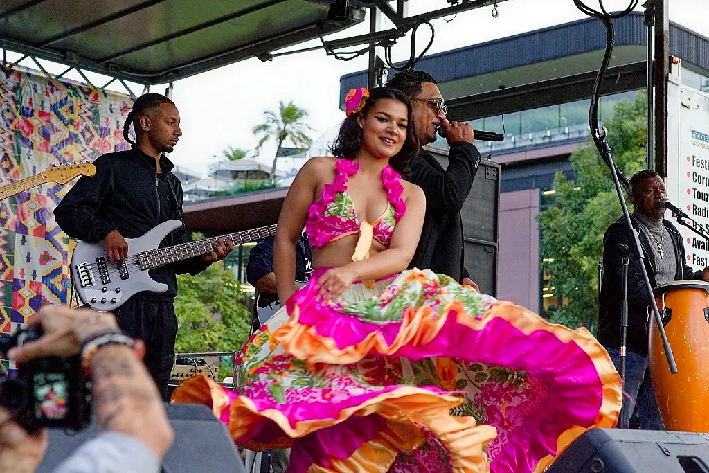 Woman in vibrant pink floral dress dancing on stage at multicultural festival.
