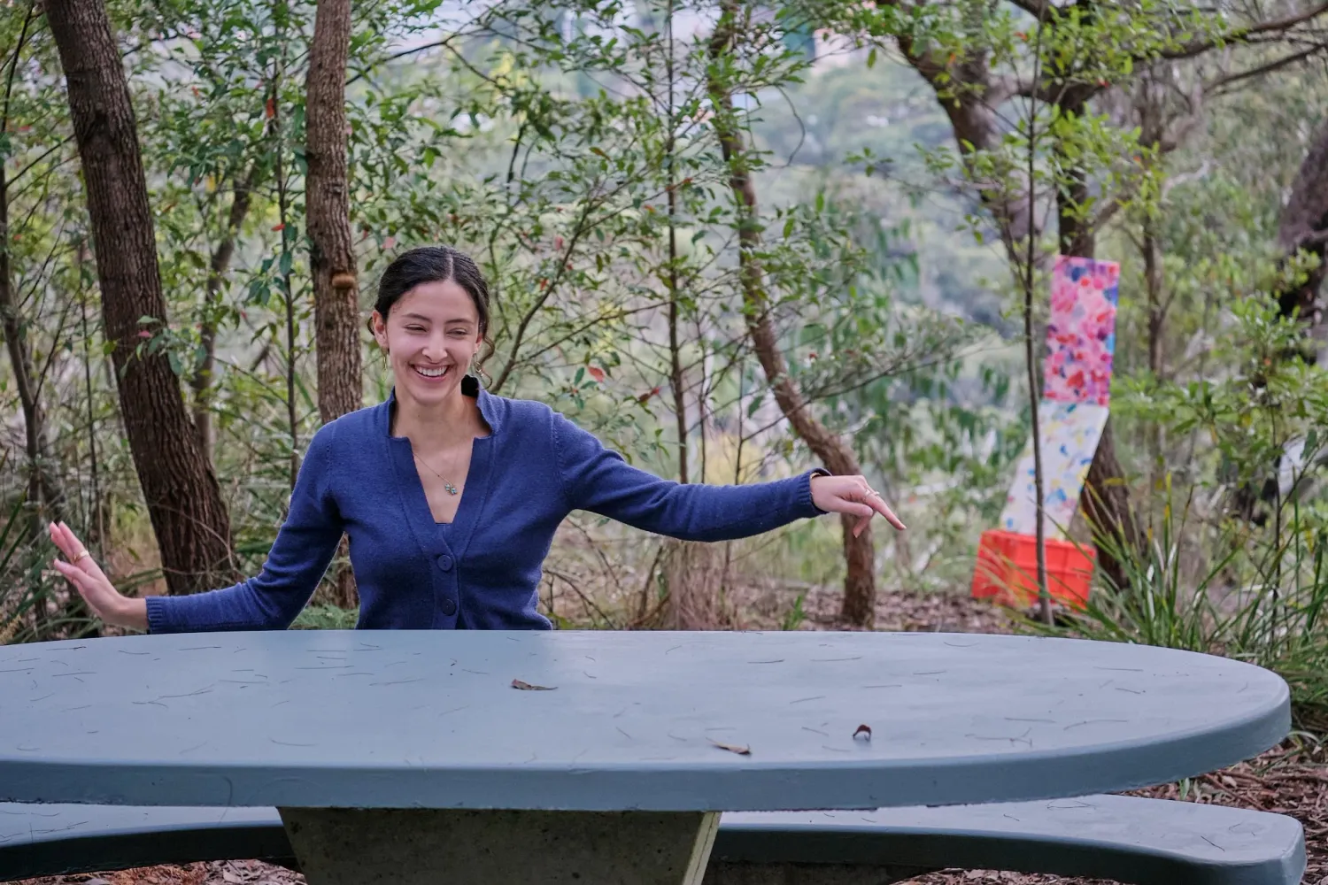 Cheerful woman in blue outfit standing at an outdoor picnic table in Australian bushland.