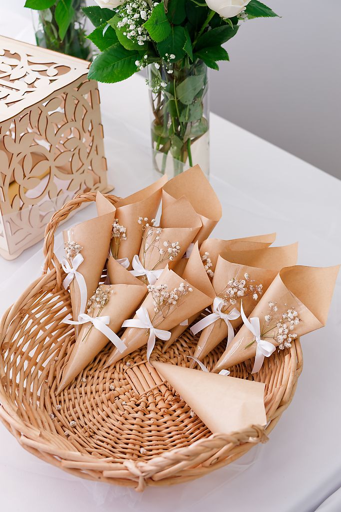 Wicker basket filled with kraft paper cones tied with white ribbon and baby's breath, beside a flower vase and laser-cut wooden box.