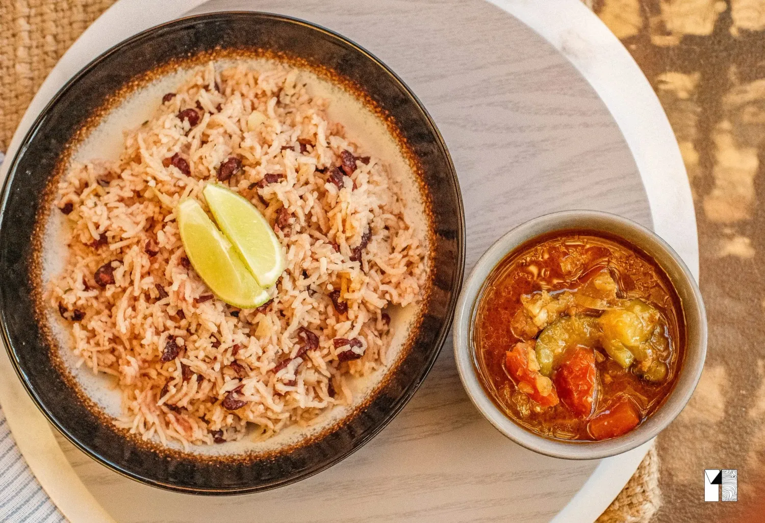 Flavorful rice dish served with a slice of lime alongside a spicy vegetable curry in a bowl.