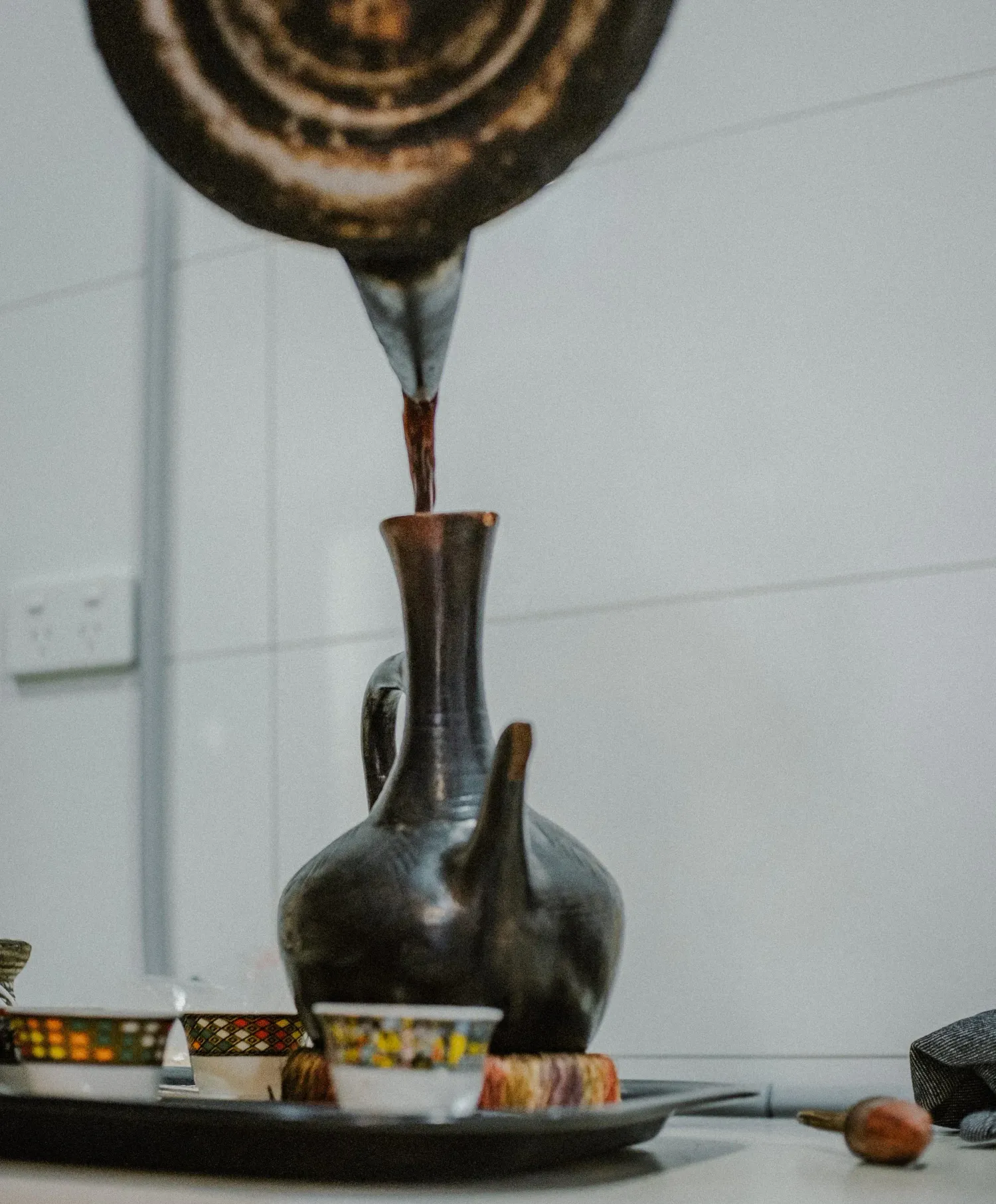Traditional Ethiopian jebena coffee pot being filled with freshly brewed dark coffee on a decorative tray.
