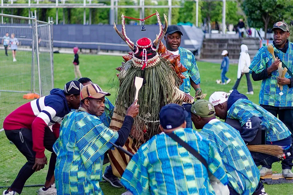 Traditional cultural ceremony with a masked dancer surrounded by performers in blue outfits.