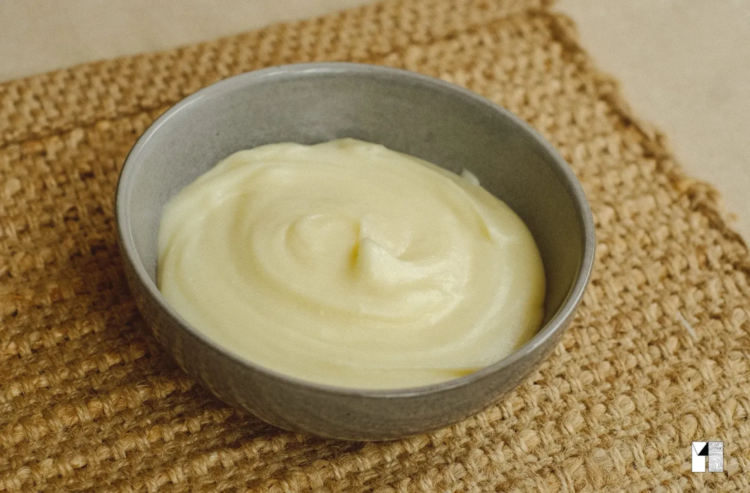 Smooth creamy white sauce swirled in a small metal bowl on a burlap surface.