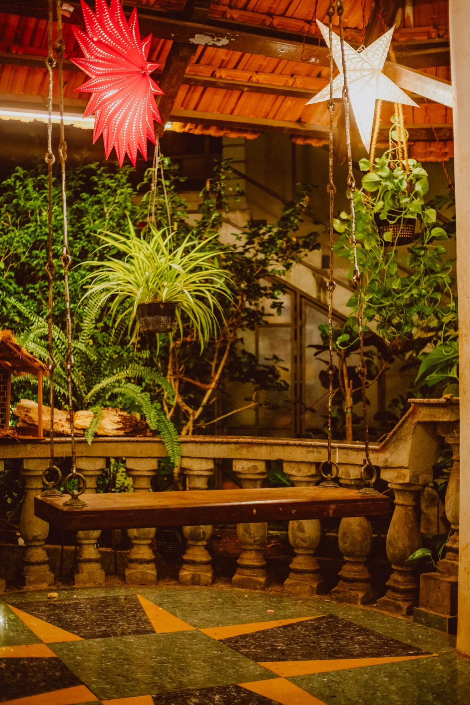 Lush indoor garden with hanging plants and decorative stars on a stone balcony with checkered floor.