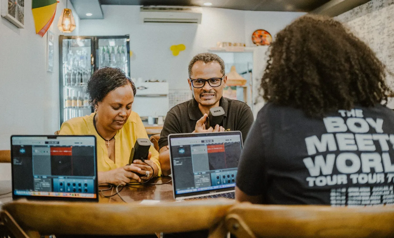 Three people smiling and working on laptops together at a wooden table in a cozy cafe.