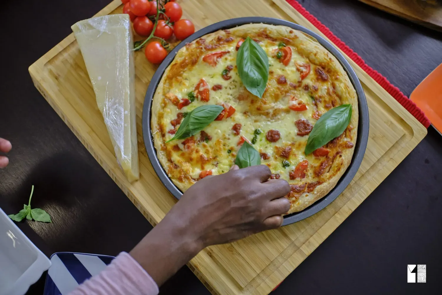 Fresh homemade pizza topped with basil, tomatoes, and melted cheese on a wooden cutting board.