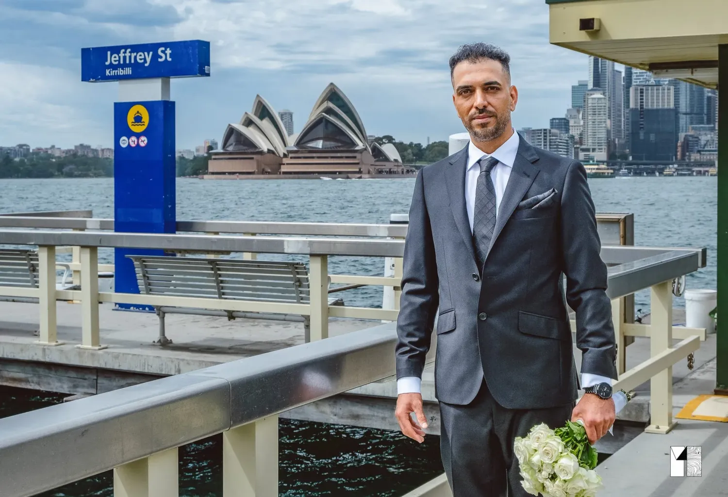 Groom in grey suit holding bouquet at Jeffrey Street Wharf with Sydney Opera House backdrop.