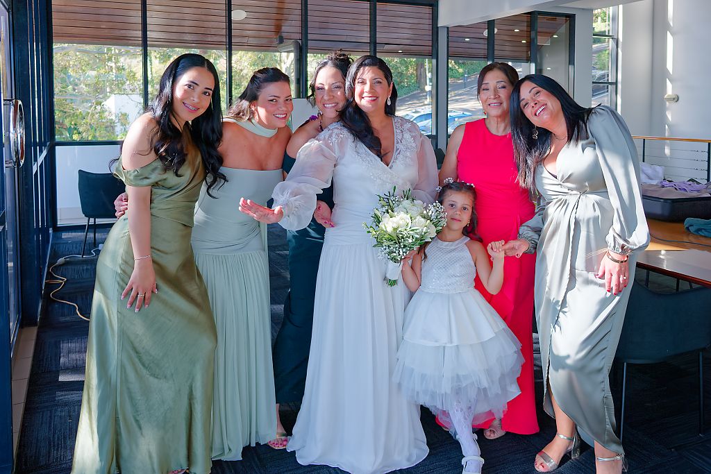 Bride in a white gown holding a bouquet poses with a flower girl and four bridesmaids in green, pink and gray dresses at a wedding.