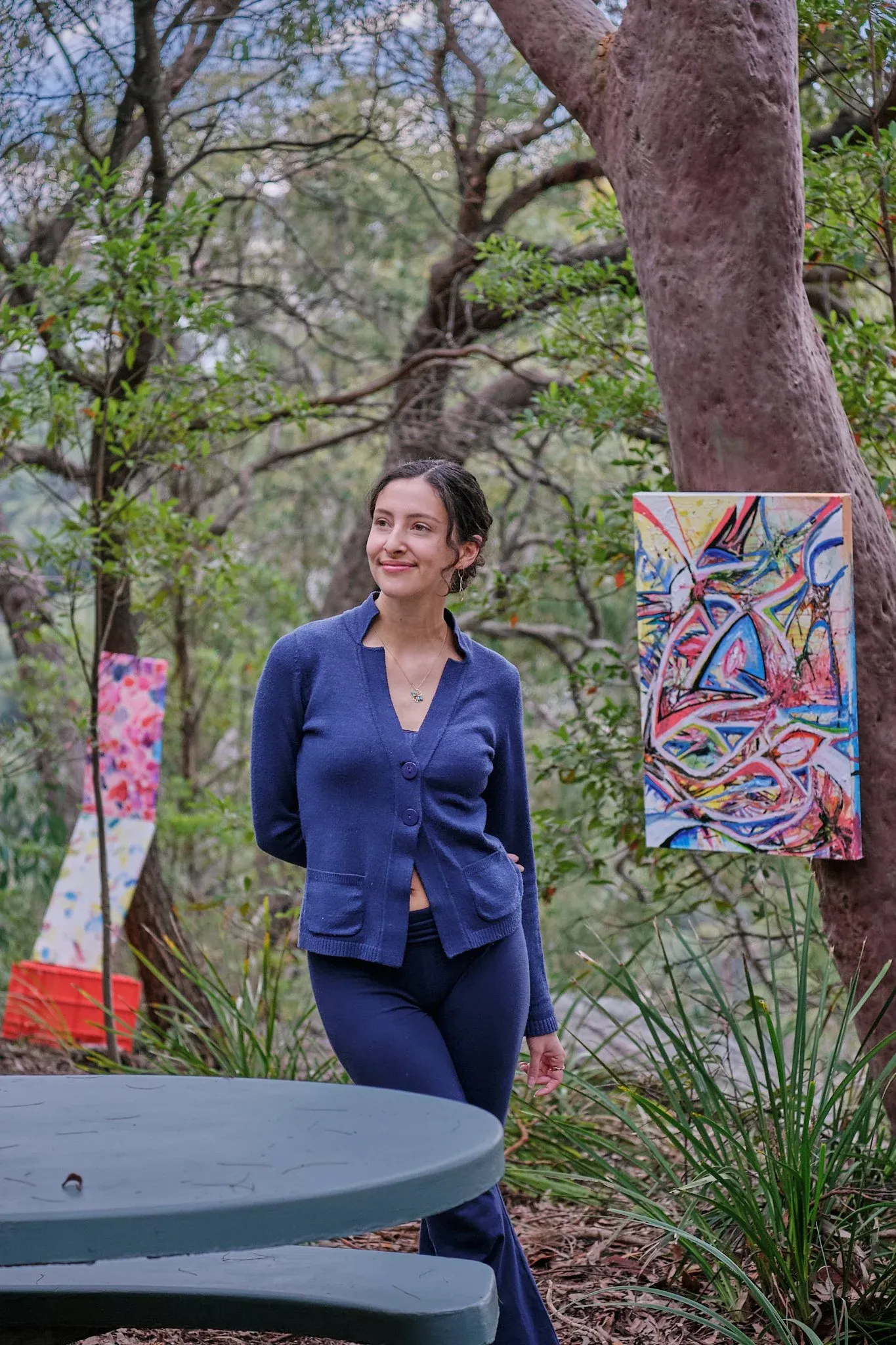 Woman in blue knit suit smiling beside colorful abstract artwork hung on tree.