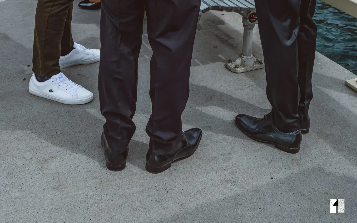 Close-up of three men's dress shoes and pants at waterfront wedding.