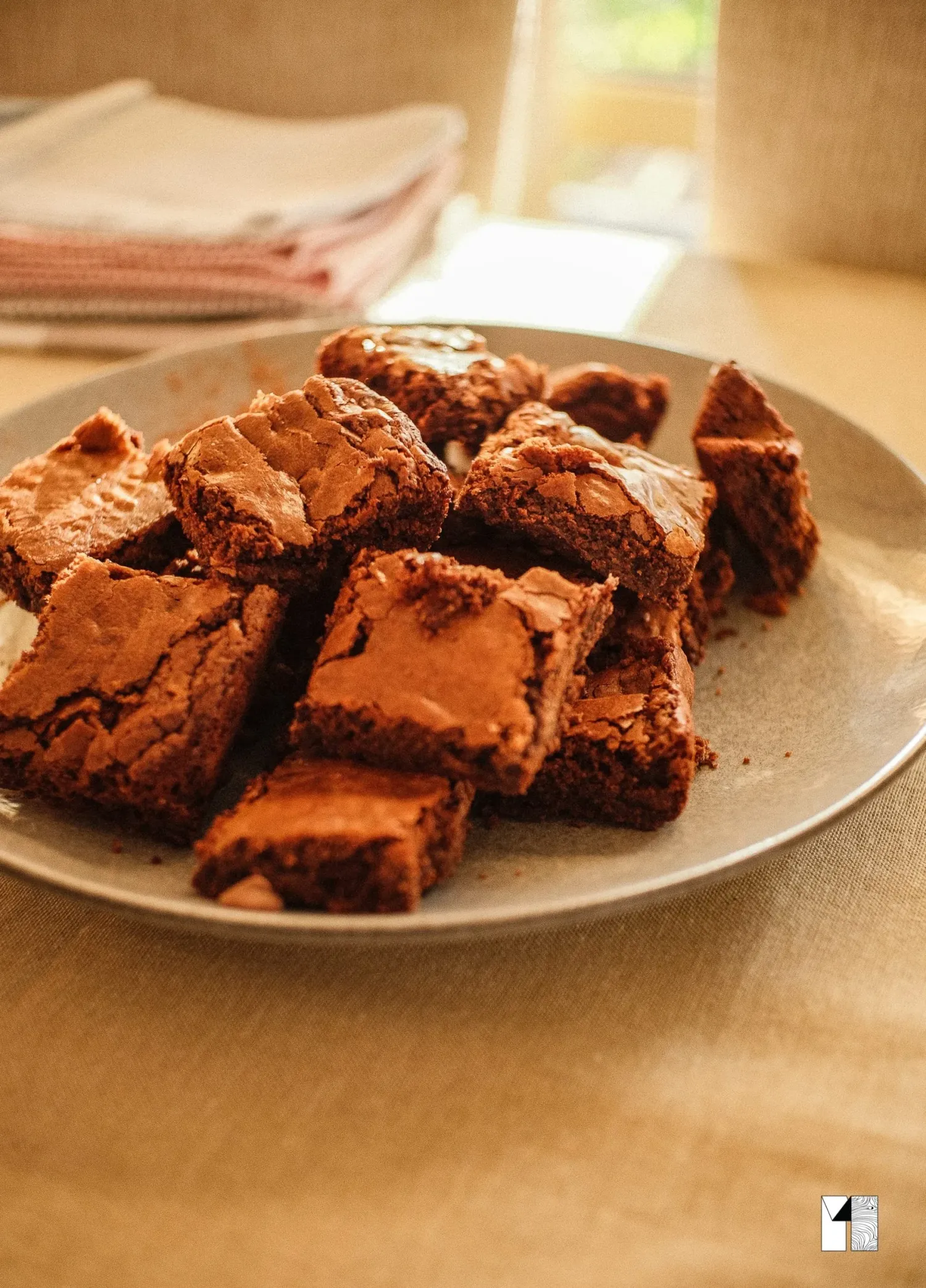Stack of rich chocolate brownies cut into squares on a plate in natural light.