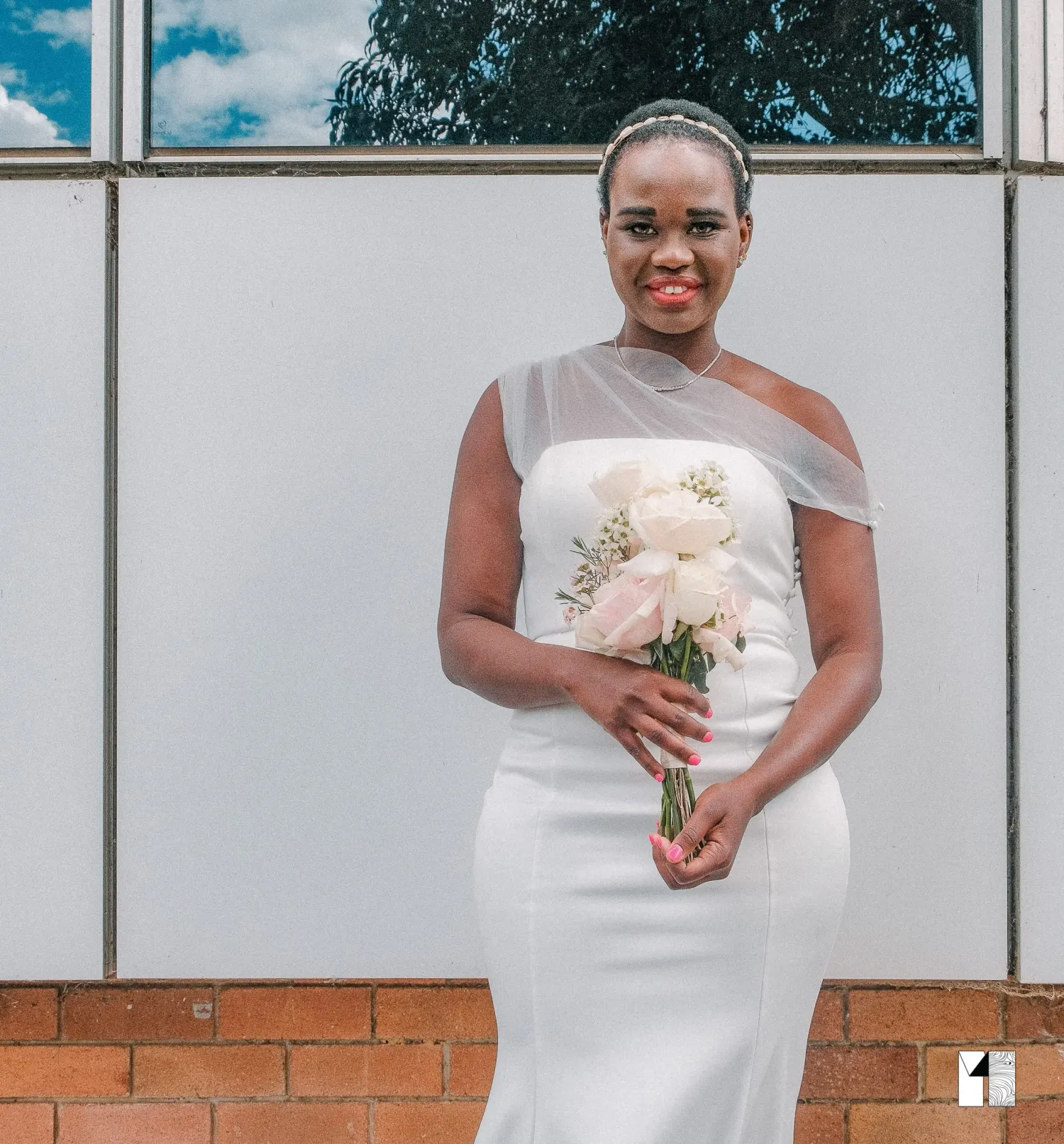 Elegant bride in a white one-shoulder wedding dress holding a bouquet of blush pink flowers.
