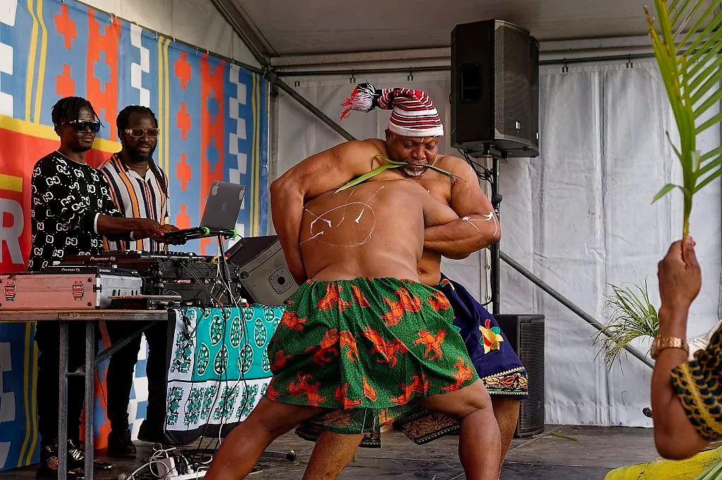 Traditional African dancer performing energetically on stage in colorful attire at an outdoor cultural festival.