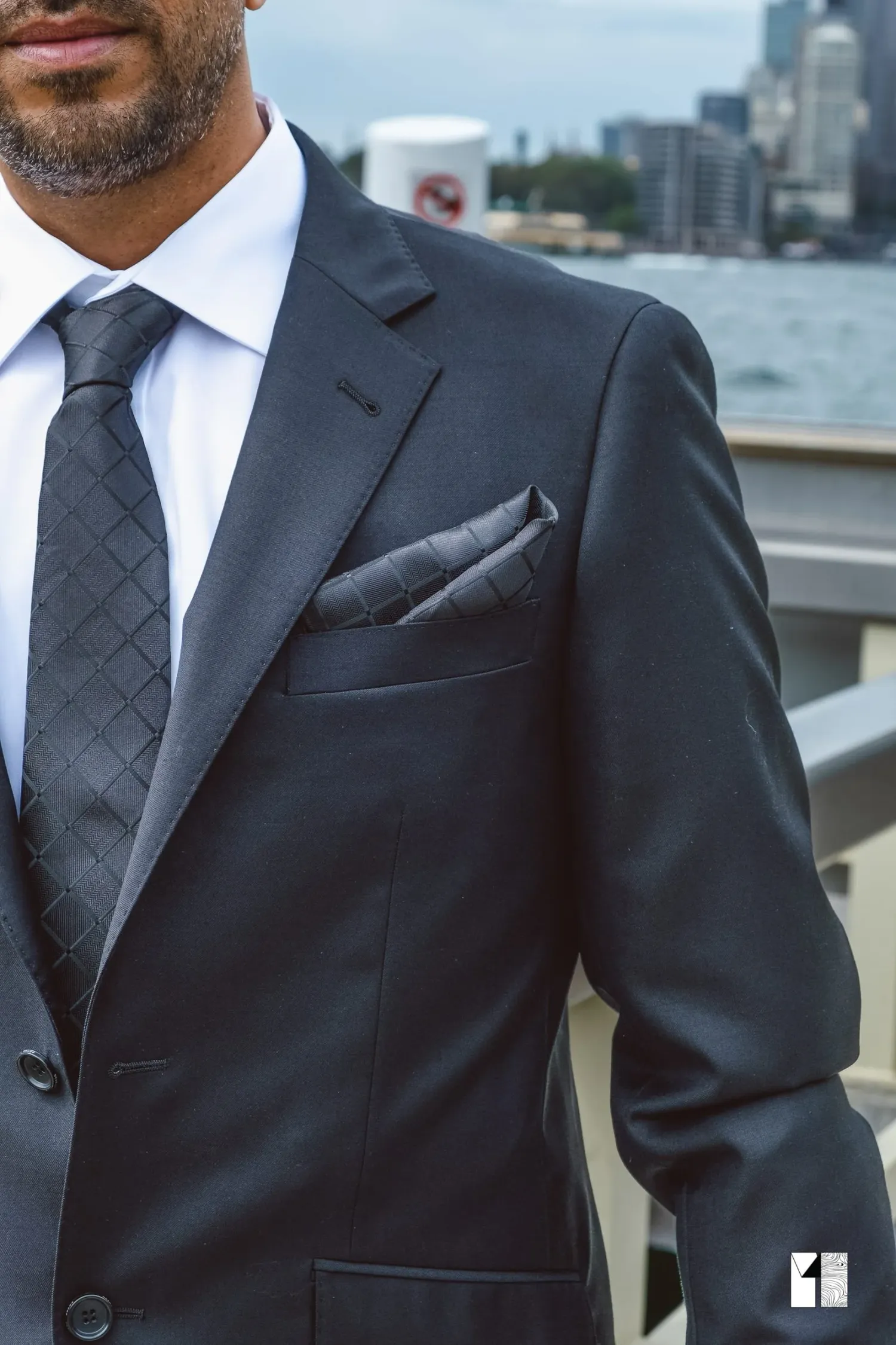 Close-up of groom in charcoal suit with patterned tie and pocket square by harbour.