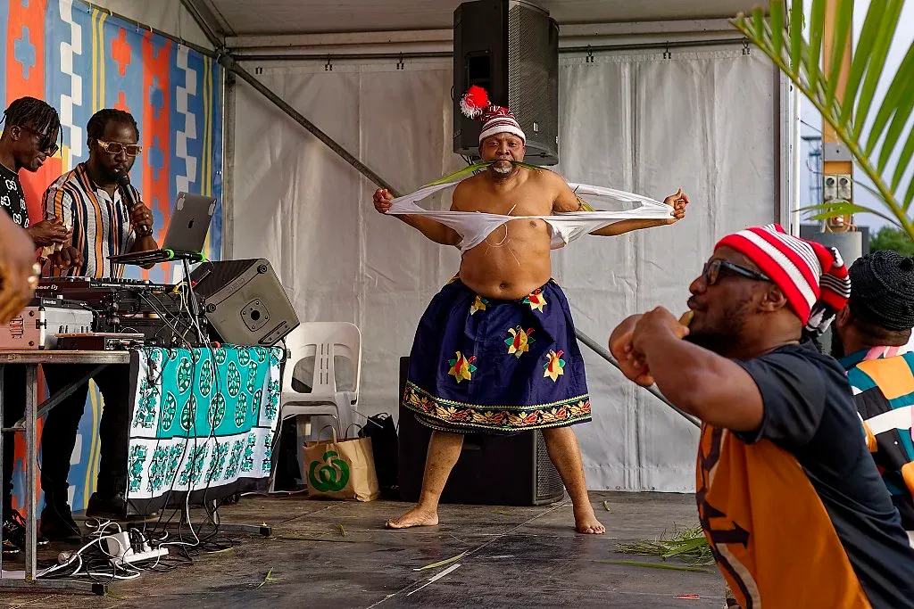 A traditional dancer in a blue skirt and feathered hat performs on stage at a cultural event.