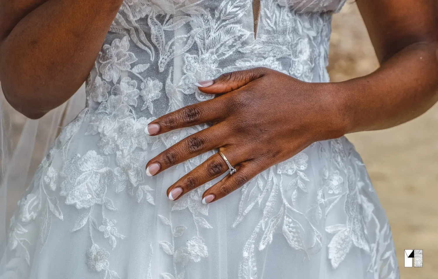 Close-up of a bride's hand displaying wedding rings on a white lace bridal gown.