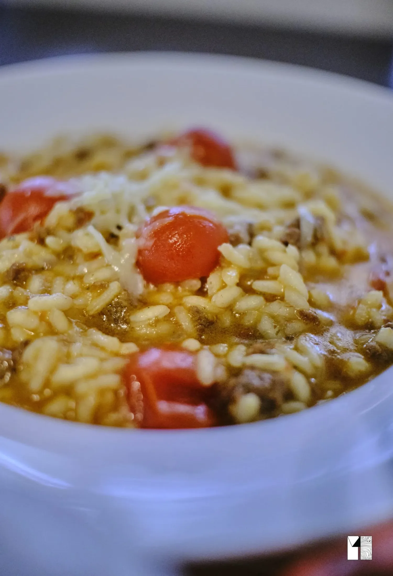 Hearty rice soup with cherry tomatoes and melted cheese served in a white ceramic bowl.