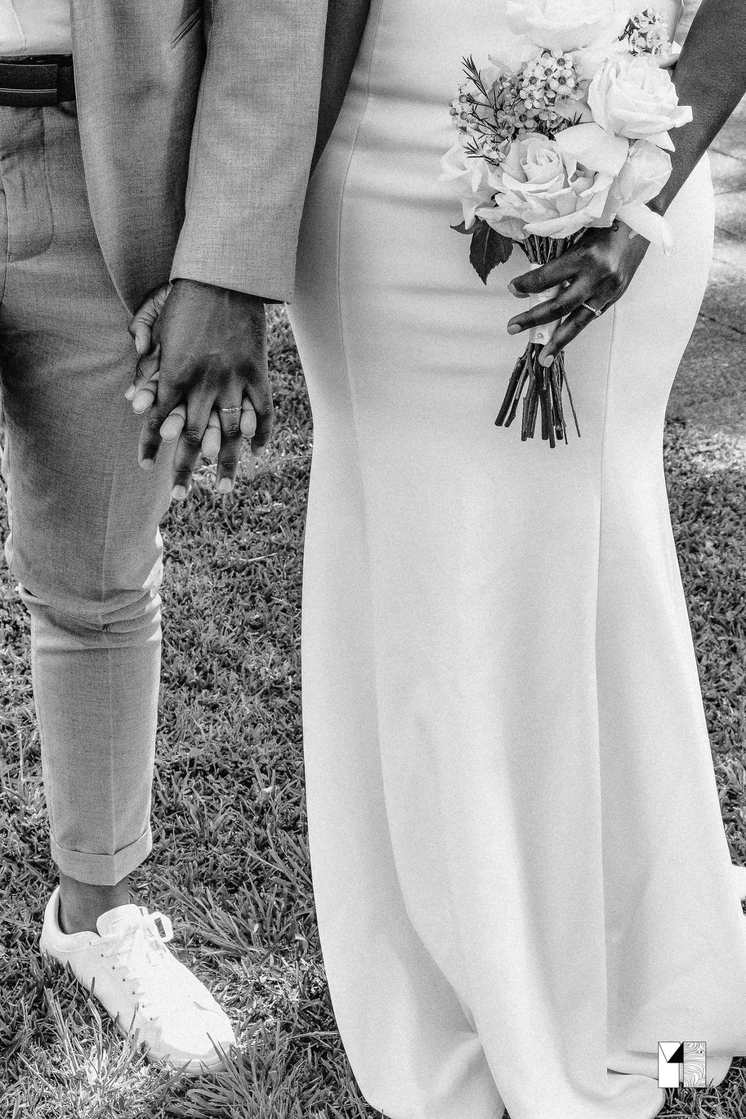 Black and white photo of bride and groom holding hands, bride holding a rose bouquet.
