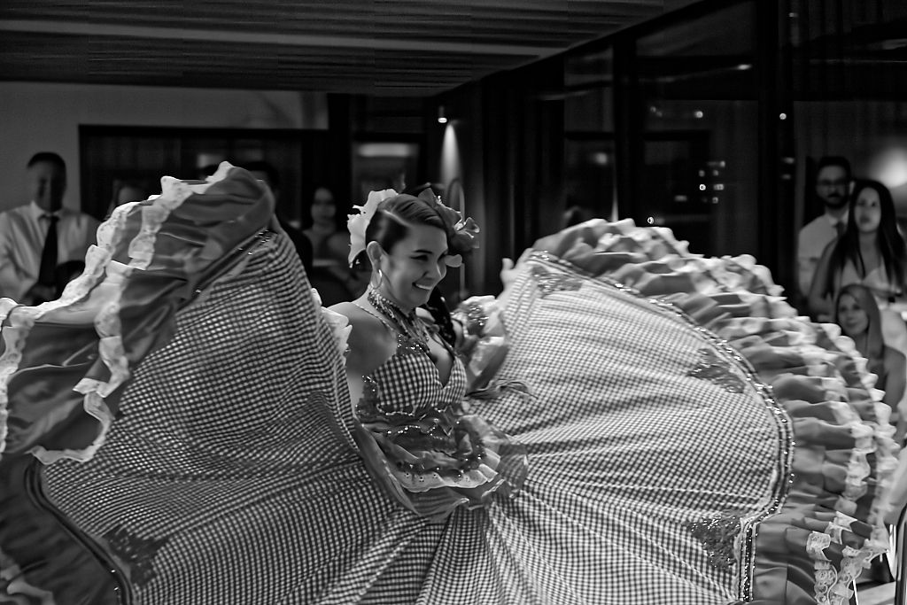 Folk dancer in a ruffled gingham dress twirls her wide skirt while an audience watches in the background.