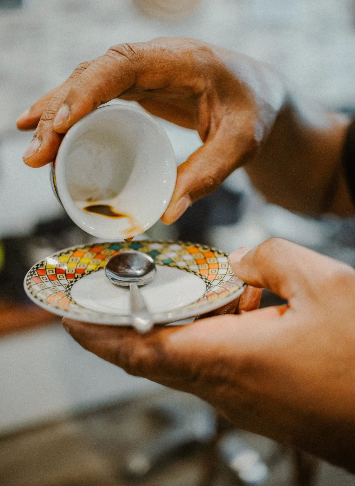 Hands pouring Ethiopian coffee from a small decorative cup onto a colorful patterned saucer.