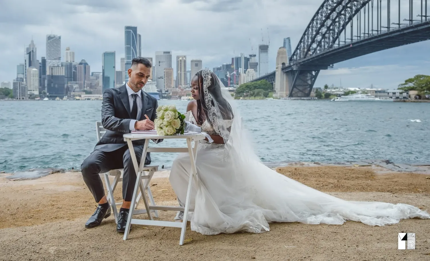 Bride and groom signing wedding documents by Sydney Harbour Bridge on a cloudy day.