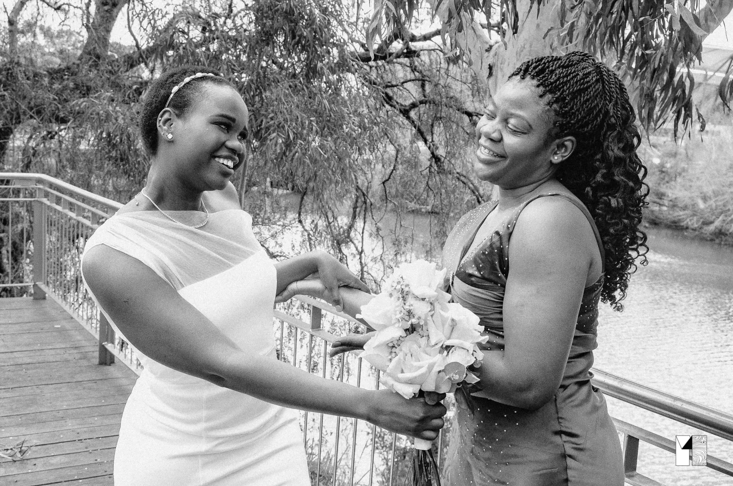 Black and white photo of bride sharing a joyful moment with a female guest on a wooden bridge.