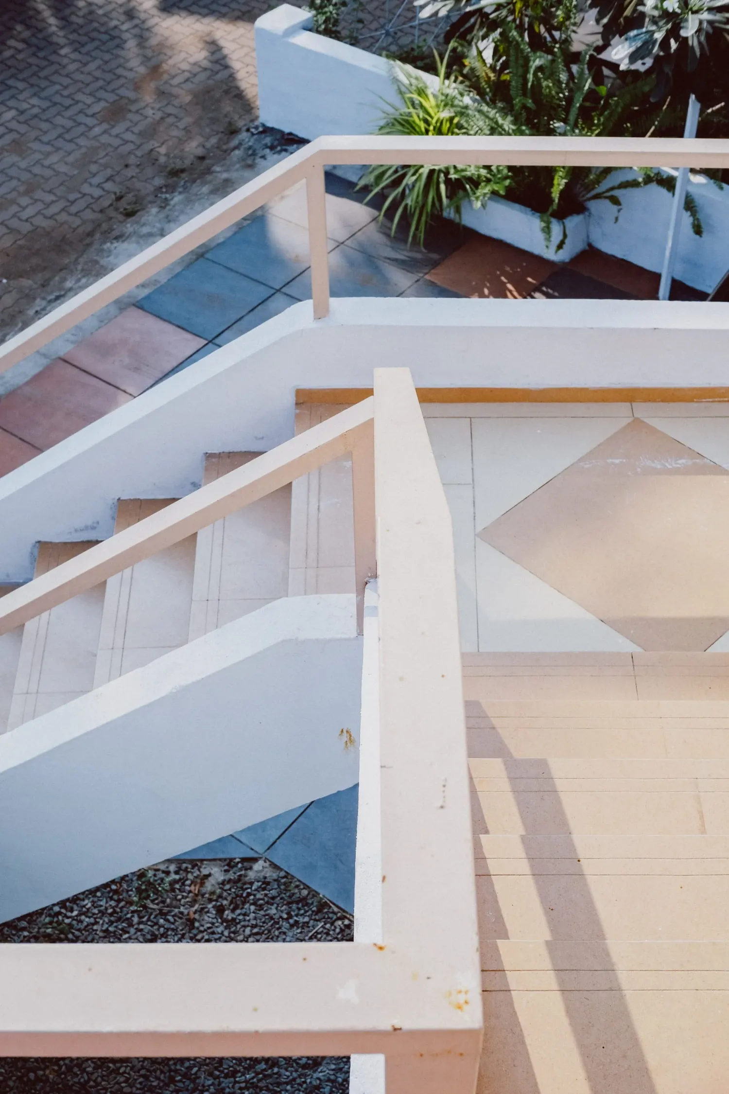 Aerial view of white modern staircase with wooden railings and tropical plants on landing.