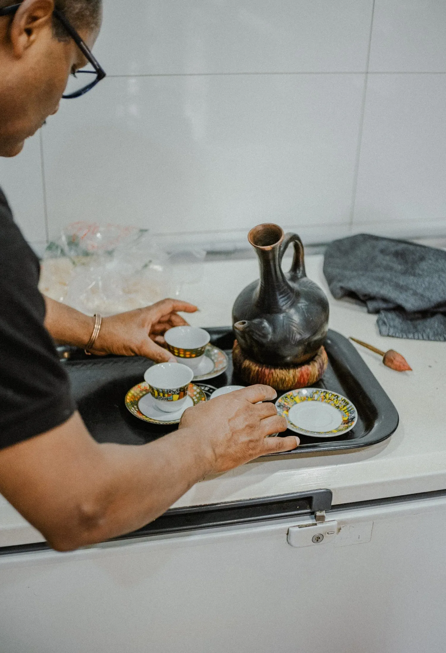 Person arranging traditional Ethiopian coffee ceremony set with black clay jebena and decorative cups.