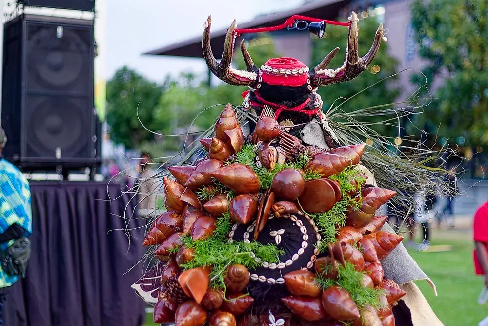 An elaborate traditional costume adorned with shells, antlers, and greenery at a cultural festival.