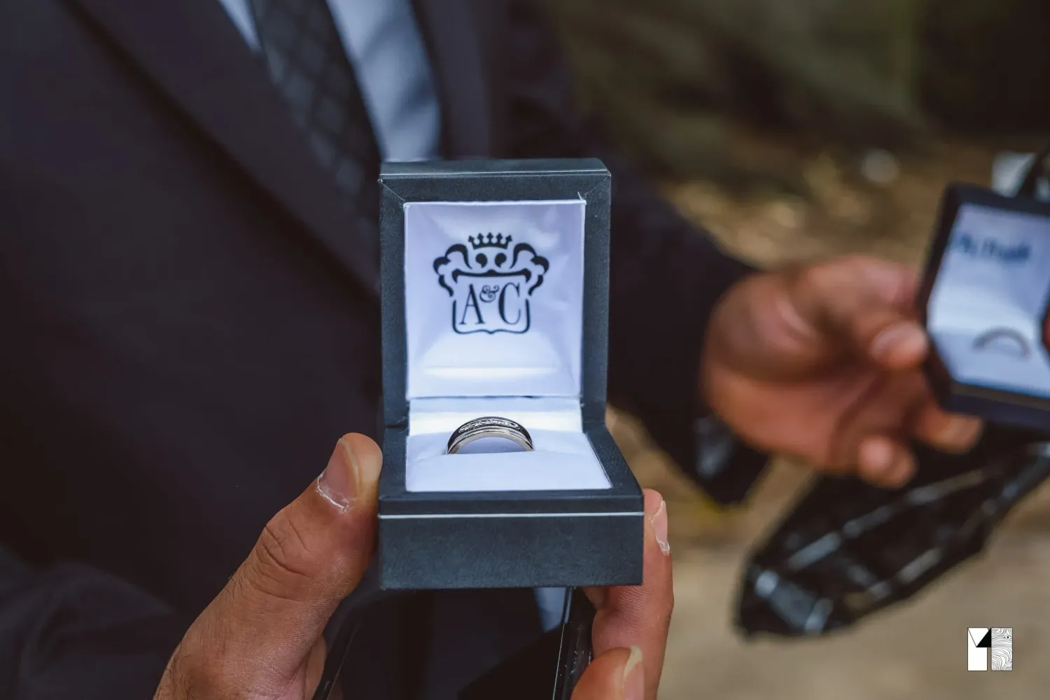 Groom's dark wedding band displayed in luxury jewelry box at outdoor ceremony.