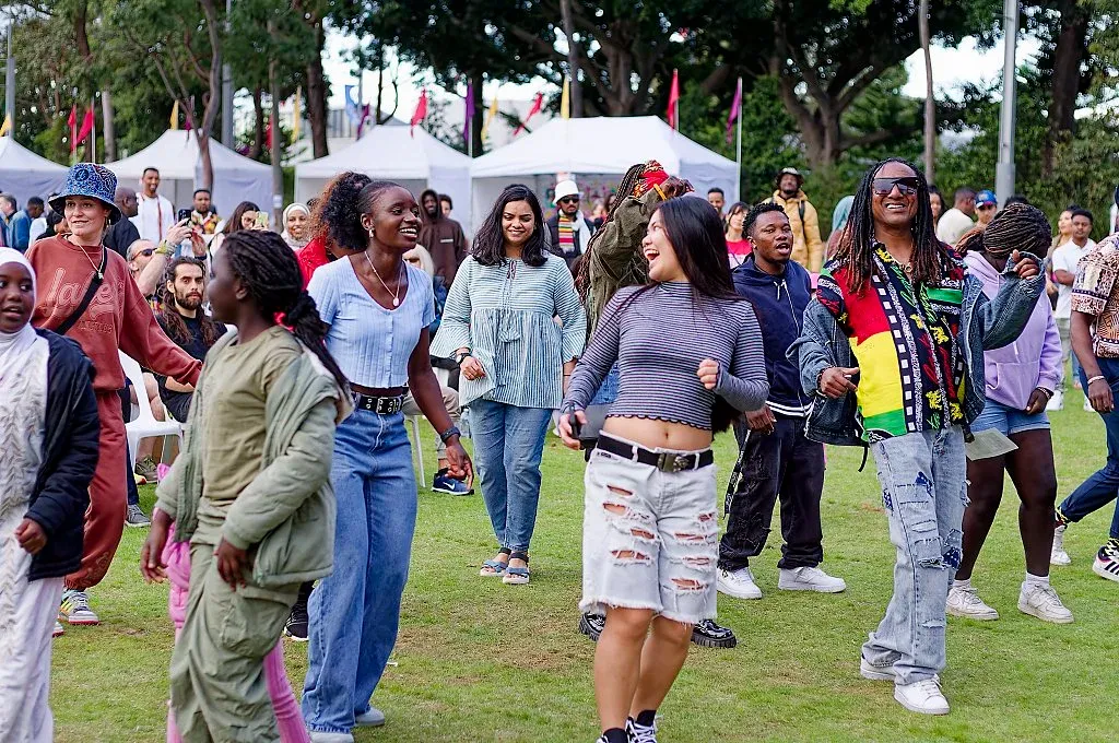 Diverse crowd of people dancing together on a grass lawn at a vibrant outdoor cultural festival.