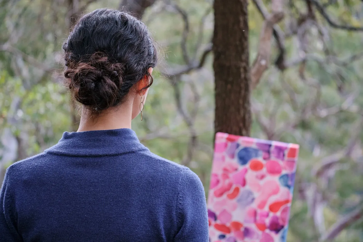 Back view of a woman with a bun hairstyle looking at a colorful abstract painting outdoors.