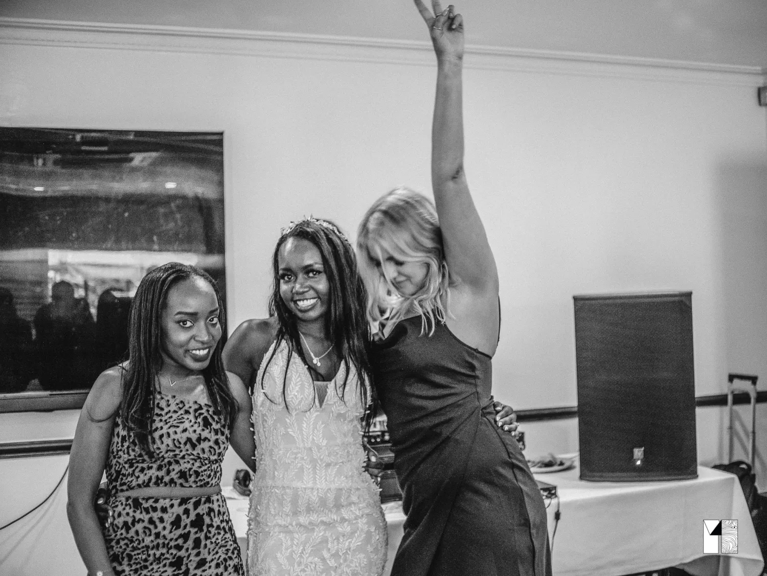 Three women celebrate joyfully at wedding reception, one raising her arm in excitement.
