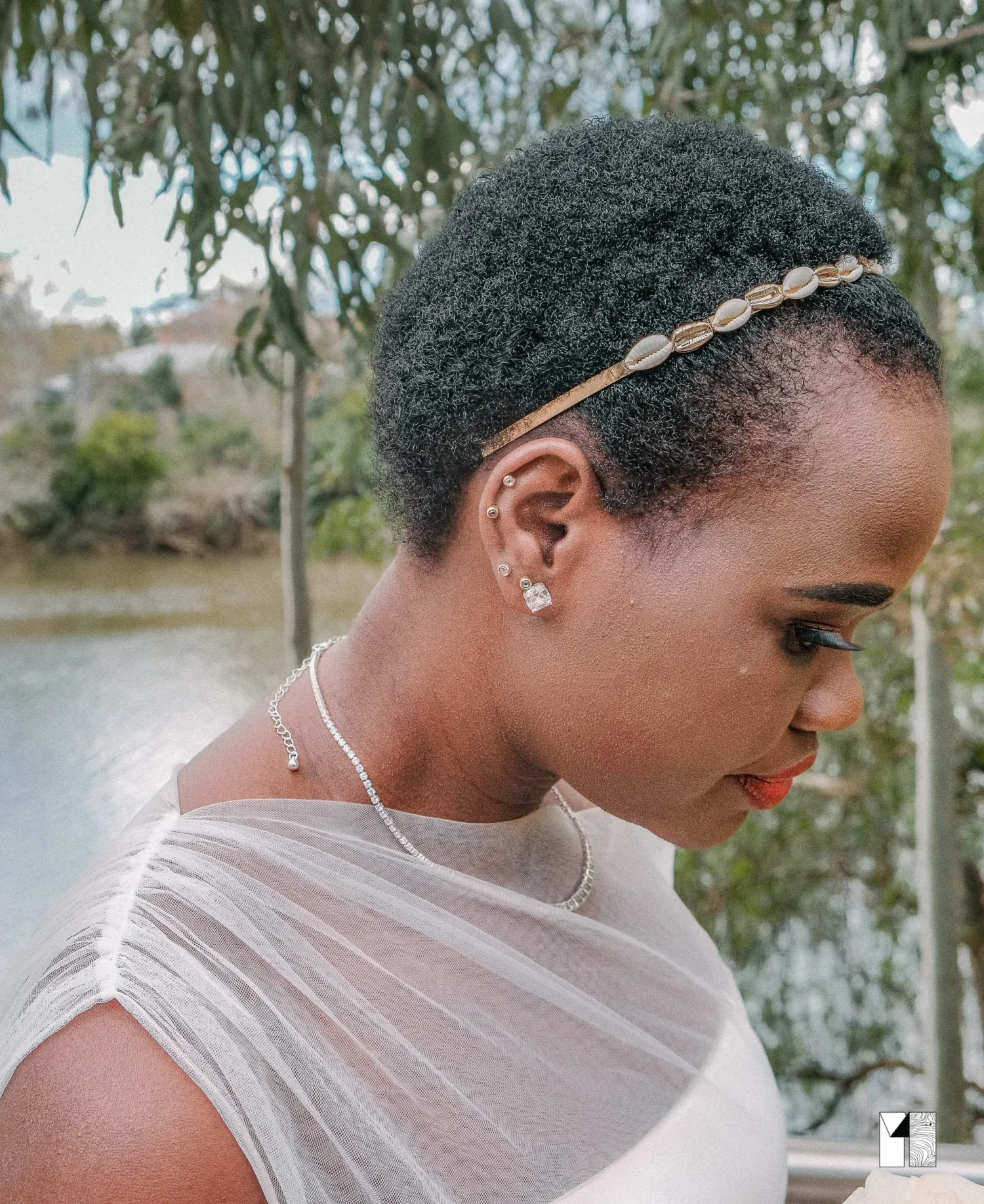 Side profile of African bride with natural hair, gold headband, pearl earrings and sheer white dress.