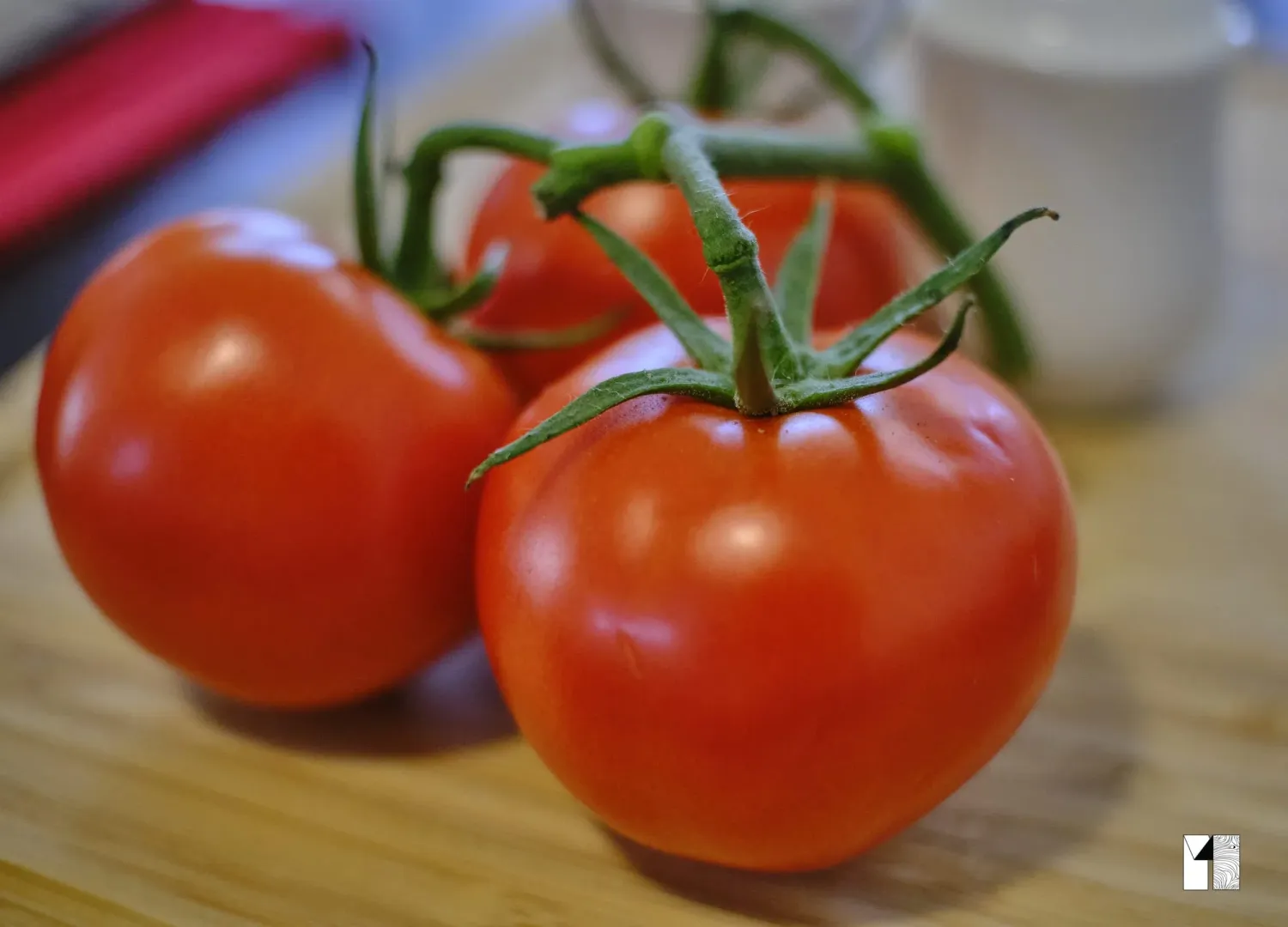 Three fresh ripe red tomatoes on the vine on a wooden cutting board.