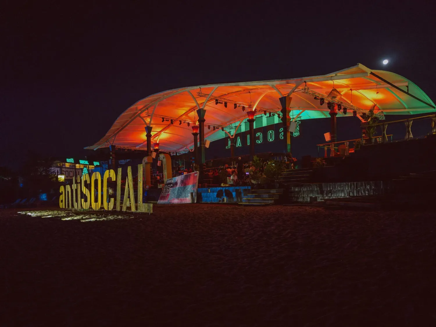 Colorful illuminated AntiSocial beach venue glowing with orange and green lights at night in Goa.